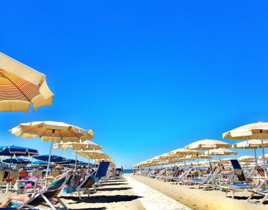 Spiaggia soleggiata con ombrelloni e lettini, cielo azzurro brillante.