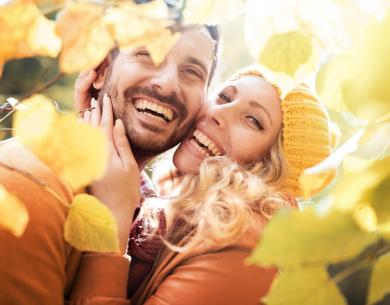 Coppia felice tra foglie autunnali, sorridenti e abbracciati.