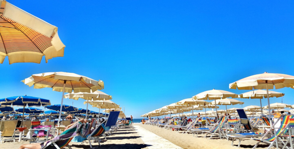 Spiaggia soleggiata con ombrelloni e lettini, cielo azzurro brillante.